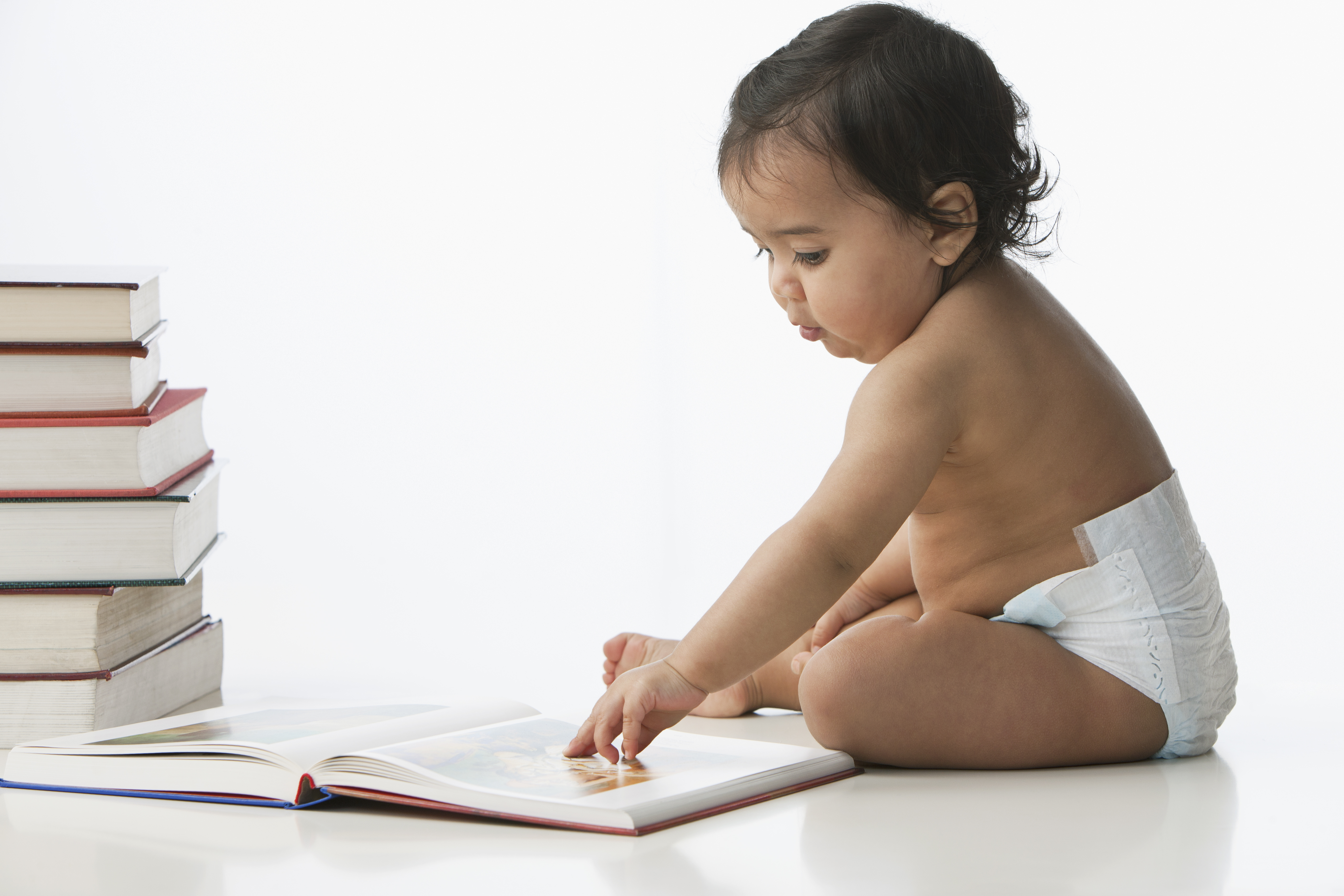 Un bebé sentado cerca de una pila de libros juega con las páginas de un libro abierto.