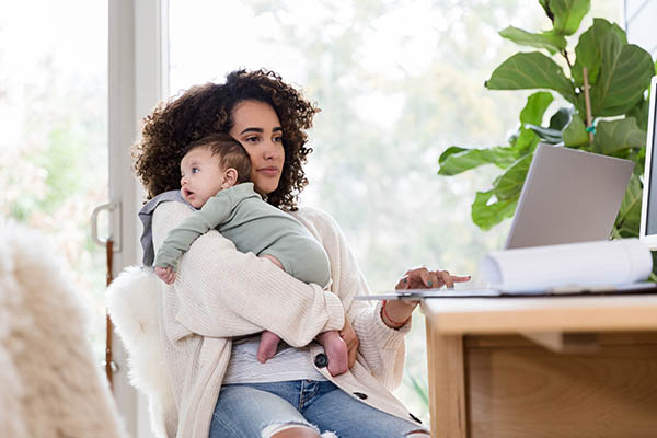 A young mother holds her baby over her shoulder and searches for health information on her laptop computer.