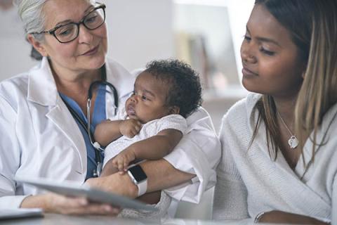 Una proveedora de atención médica acuna a un bebé mientras muestra los resultados de las pruebas de detección del recién nacido a la madre del bebé.